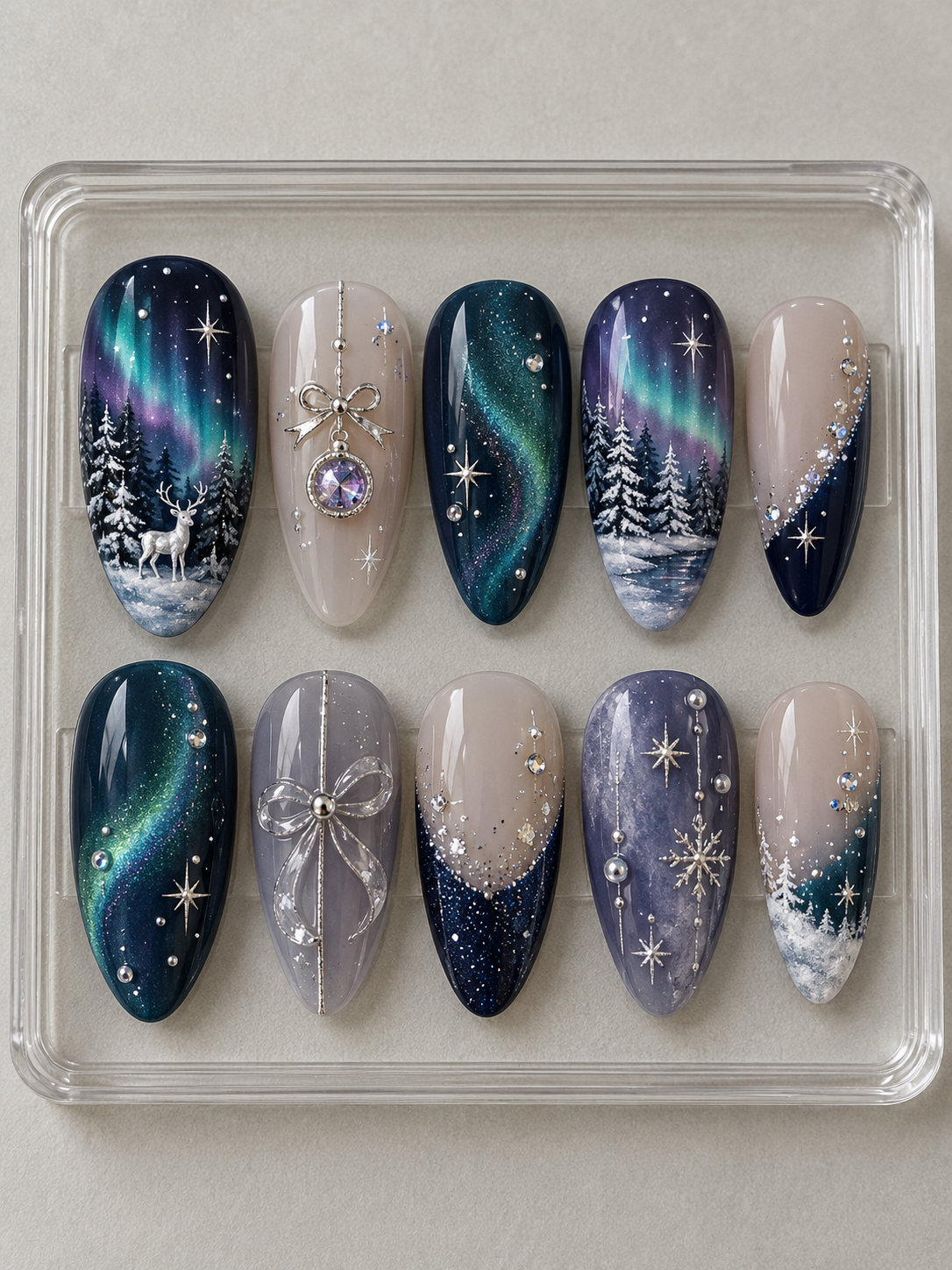 Ten navy, teal, violet and nude Christmas press-on nails with aurora skies, snowy pines, deer, silver-colour bows, stars and crystal-look accents.