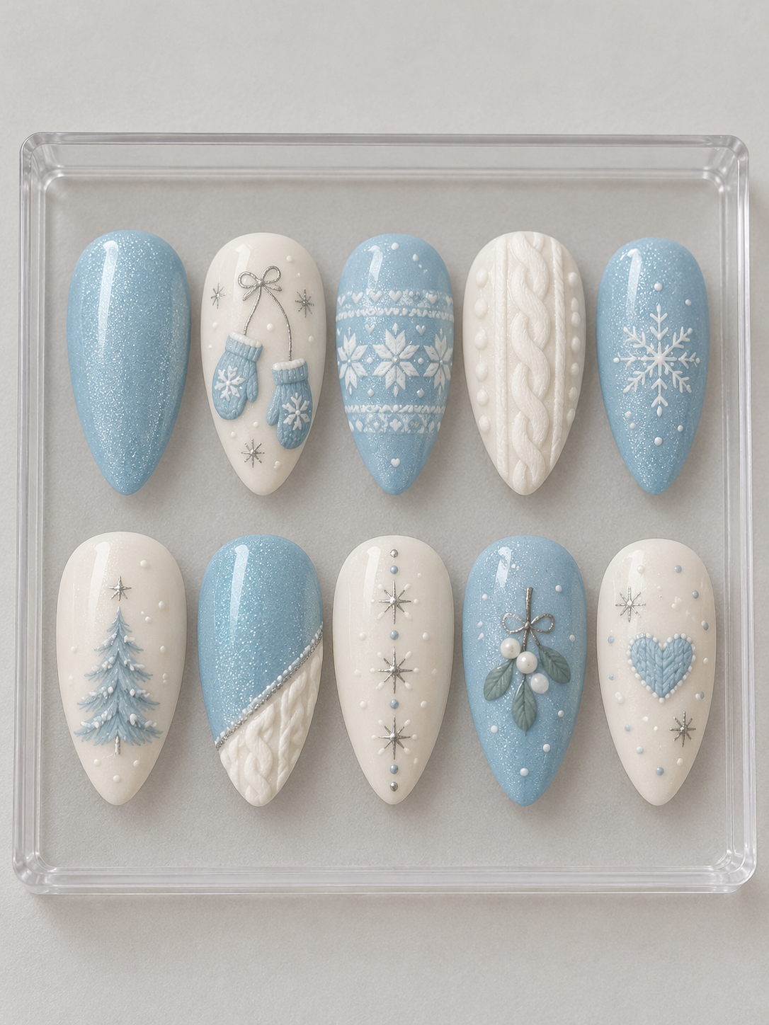 AI design mockup: Ten pale-blue and ivory Christmas press-on nails with mittens, cable-knit textures, fair-isle patterns, a tree and snowflakes.